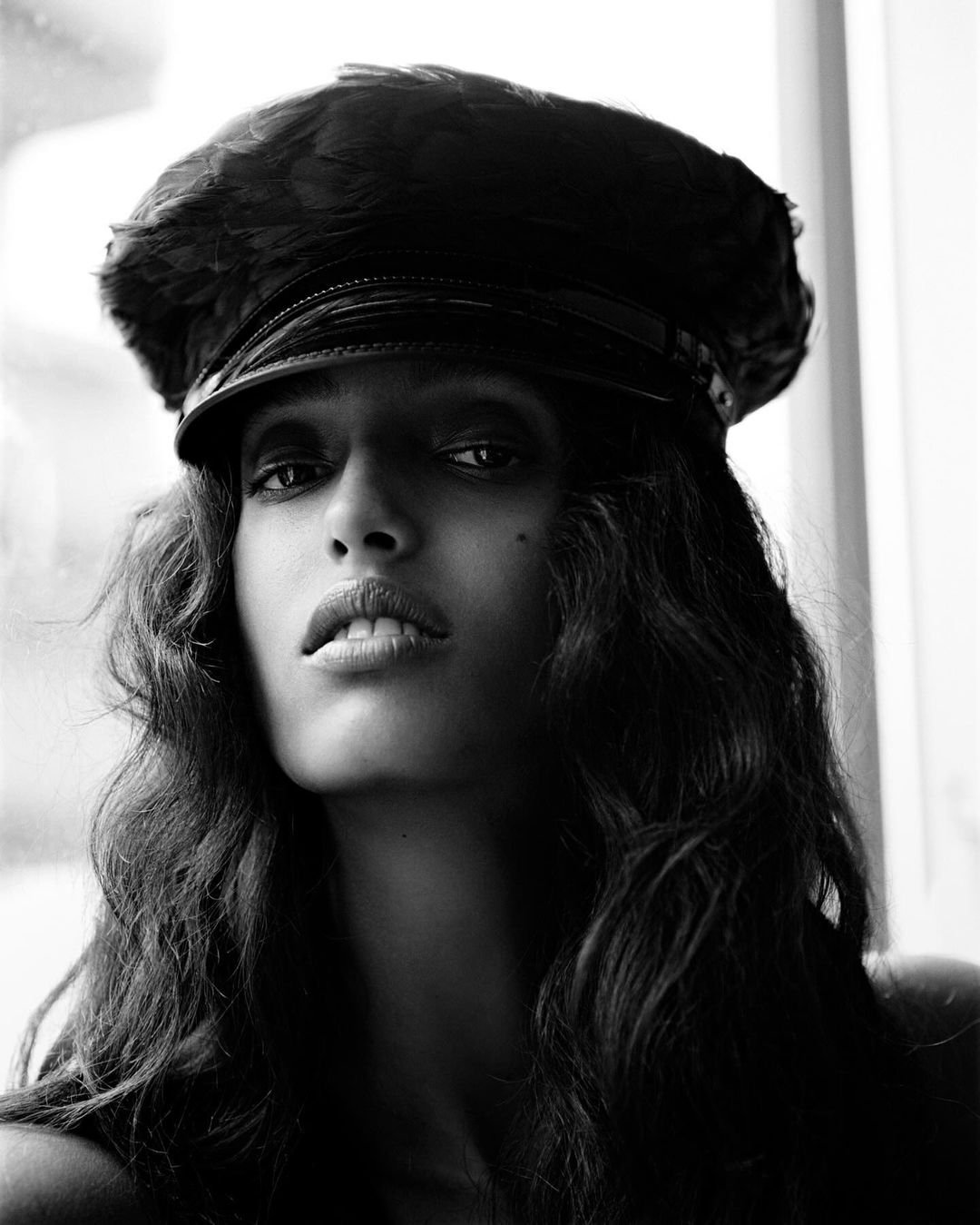 Portrait of a young woman wearing a black military-style cap, captured in a monochrome photograph with soft, diffused light.