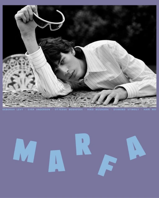 Black and white fashion shot of a young male model with sunglasses on a table, posing outdoors in a patterned shirt, with text overlay.