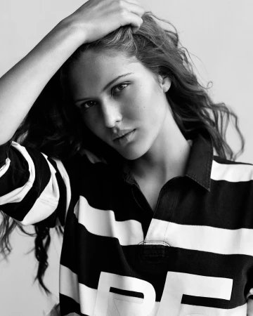 Black and white portrait of a woman wearing a striped polo shirt with her hand raised to her long wavy hair.
