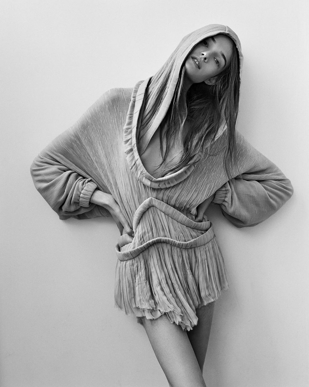 Monochrome portrait of a woman with a hooded dress in a photo studio, showcasing fashion-forward editorial style and posing against a neutral backdrop.