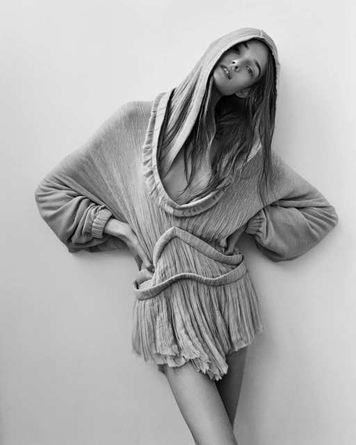 Monochrome portrait of a woman with a hooded dress in a photo studio, showcasing fashion-forward editorial style and posing against a neutral backdrop.