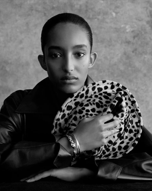 Portrait of a young woman with short dark hair in a black jacket, holding a round, spotted fur accessory. Black and white image.