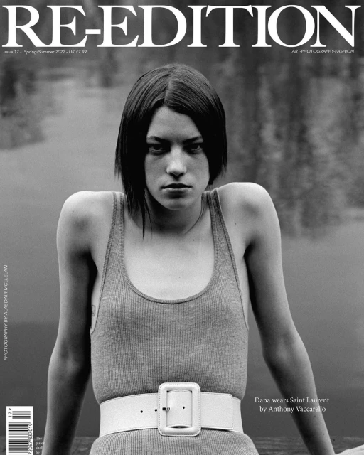 Black and white portrait of a model on a magazine cover, wearing a tank top and belt, with a blurred background of water and trees.