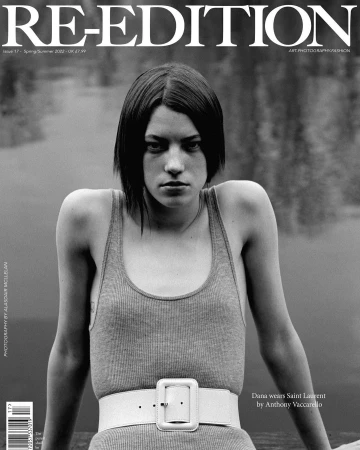 Black and white portrait of a model on a magazine cover, wearing a tank top and belt, with a blurred background of water and trees.