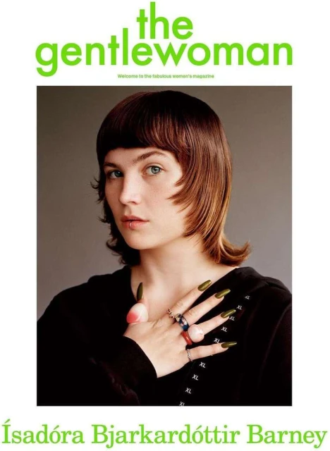Magazine cover featuring a young woman with short brown hair, rings, and olive-green nails, against a grey background and text overlay.