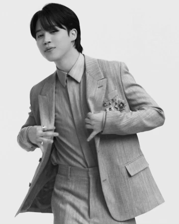 Monochrome portrait of a man in a structured suit holding jacket lapels against a plain white background
