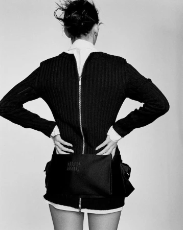 Model seen from behind wearing a black zip-up sweater over a white shirt against a plain light background