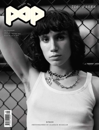 Monochrome magazine cover portrait of a person with dark hair wearing a ribbed white tank top against a chain link fence.