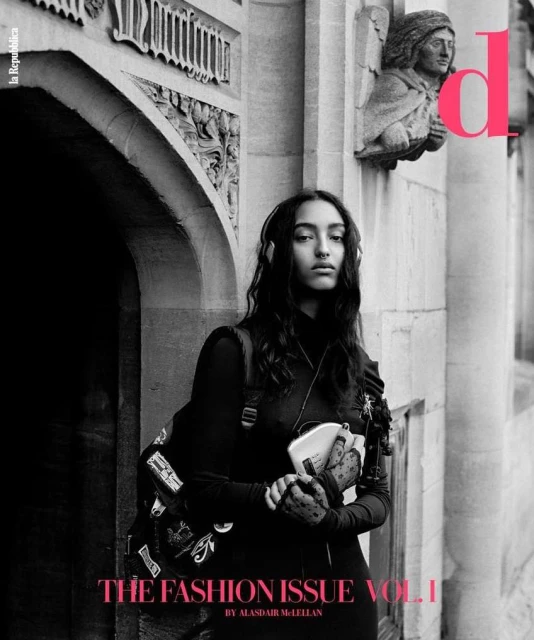 Fashion editorial shot of a woman in black attire with a backpack, captured against an ornate stone building with architectural details.