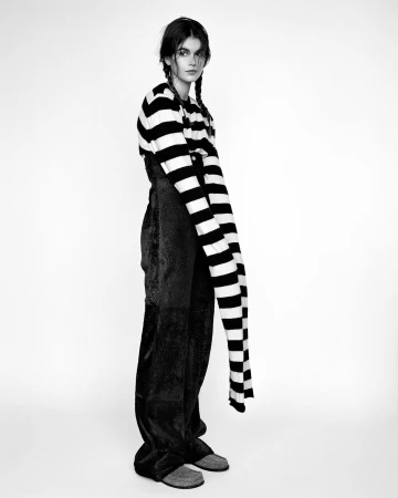 Monochrome portrait of a model with braided hair wearing a striped sweater and dark trousers against a white background
