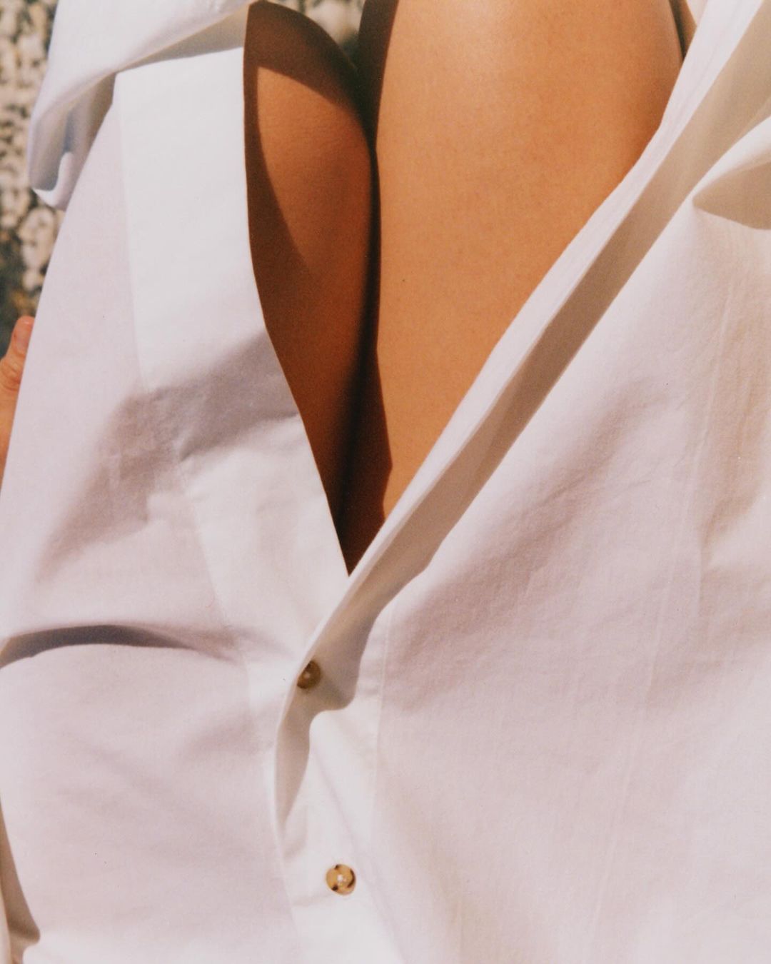 Close-up of a person's upper torso wearing an unbuttoned white collared shirt, showcasing skin and the shirt's texture.