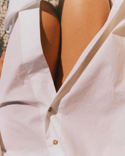Close-up of a person's upper torso wearing an unbuttoned white collared shirt, showcasing skin and the shirt's texture.