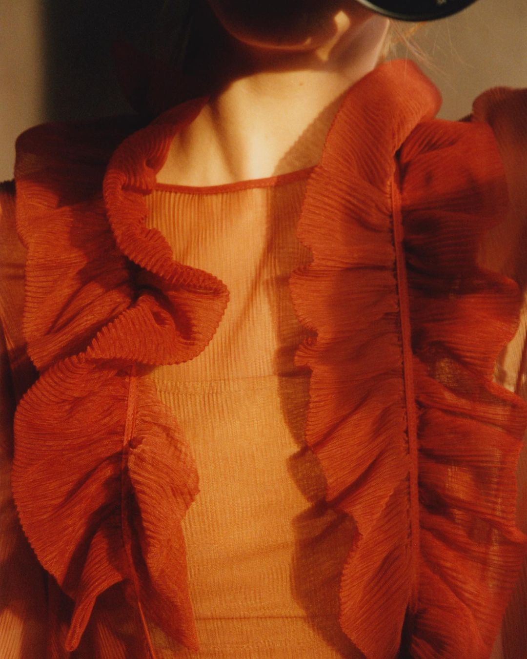 Close-up of a model wearing a red ruffled top against a neutral background in soft light, emphasizing the fabric and textures.
