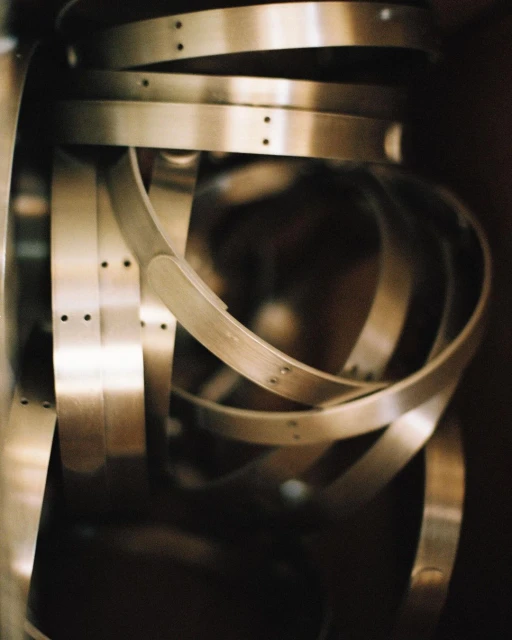 Close-up of multiple stainless steel metal bands, some curved into ring shapes, stacked in front of a dark background.