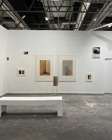 Gallery featuring framed art on white walls, a minimalist bench, and an industrial ceiling with metal beams and ductwork. Modern, clean design.