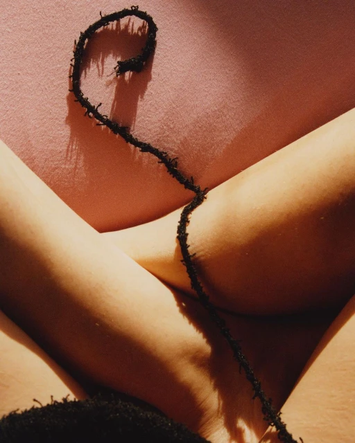 Close-up shot of a person's crossed legs and black string over a pink surface in a studio with bright, diffused lighting.