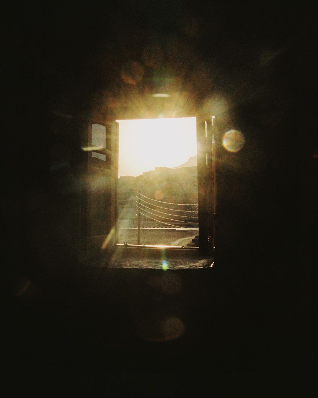 Sunlight streams through an open window, illuminating a view of a distant building and landscape in this captivating, atmospheric indoor shot.