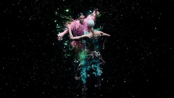 Two models in avant-garde fashion pose against a black backdrop with dispersed particles in an artistic, high-fashion presentation.