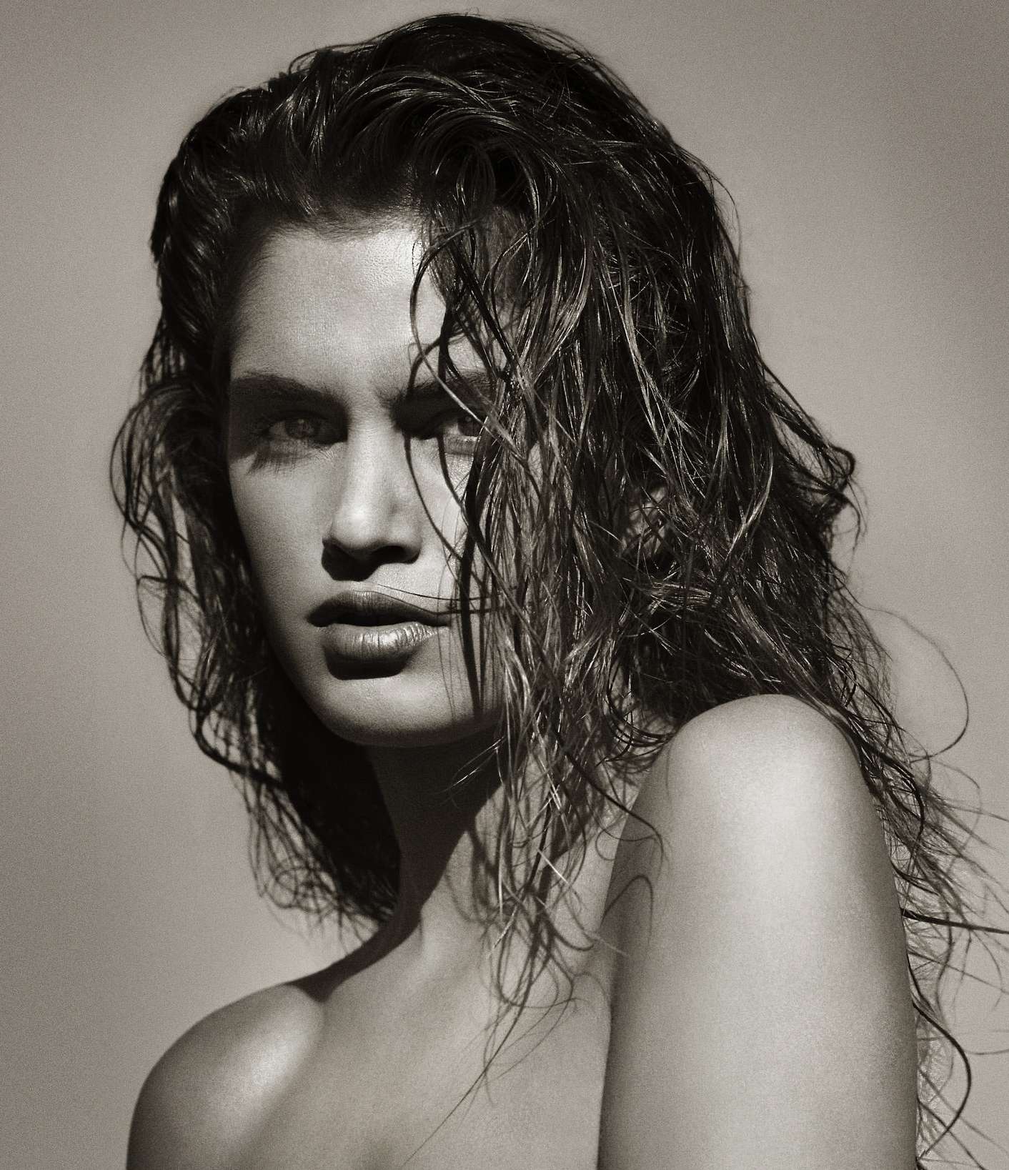 Striking portrait of a brunette adult female with wet, wavy hair and glossy lips, showcasing radiant beauty and a captivating gaze.