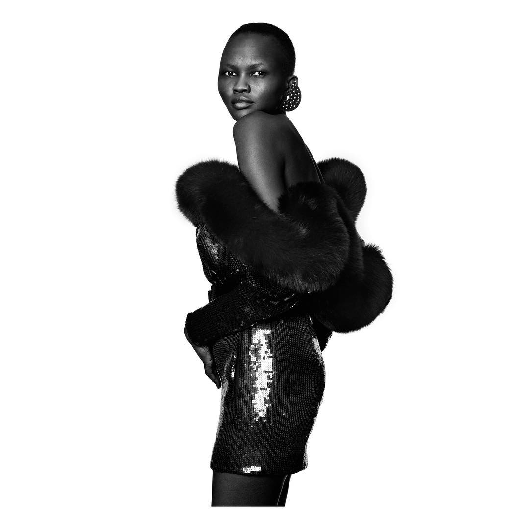 Black and white fashion portrait of a woman in a fur stole and sequined dress against a white background, accessorized with earrings.
