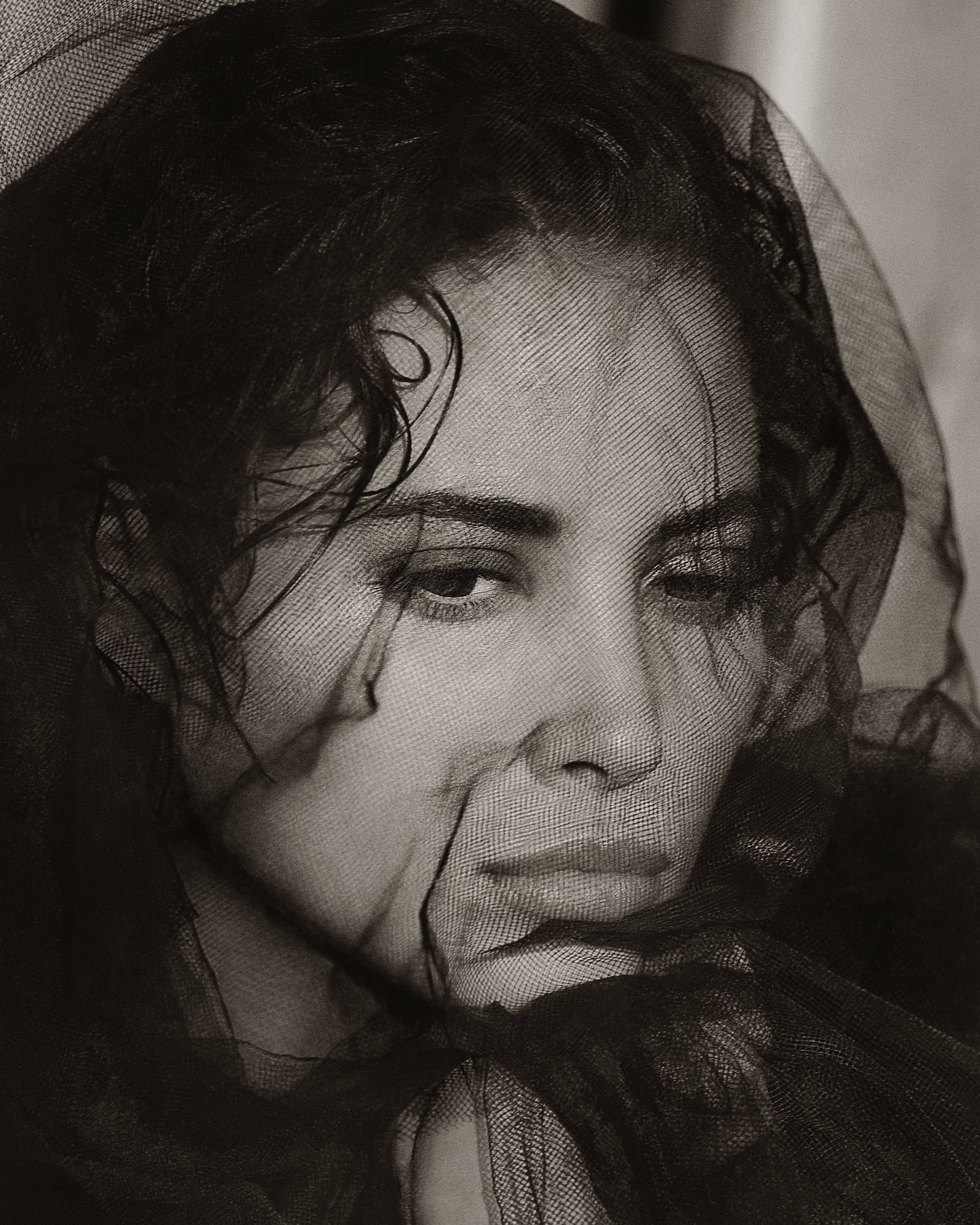 Portrait of a woman with dark hair draped in sheer black fabric, soft lighting, neutral monochrome tones, fashion, and beauty concept.