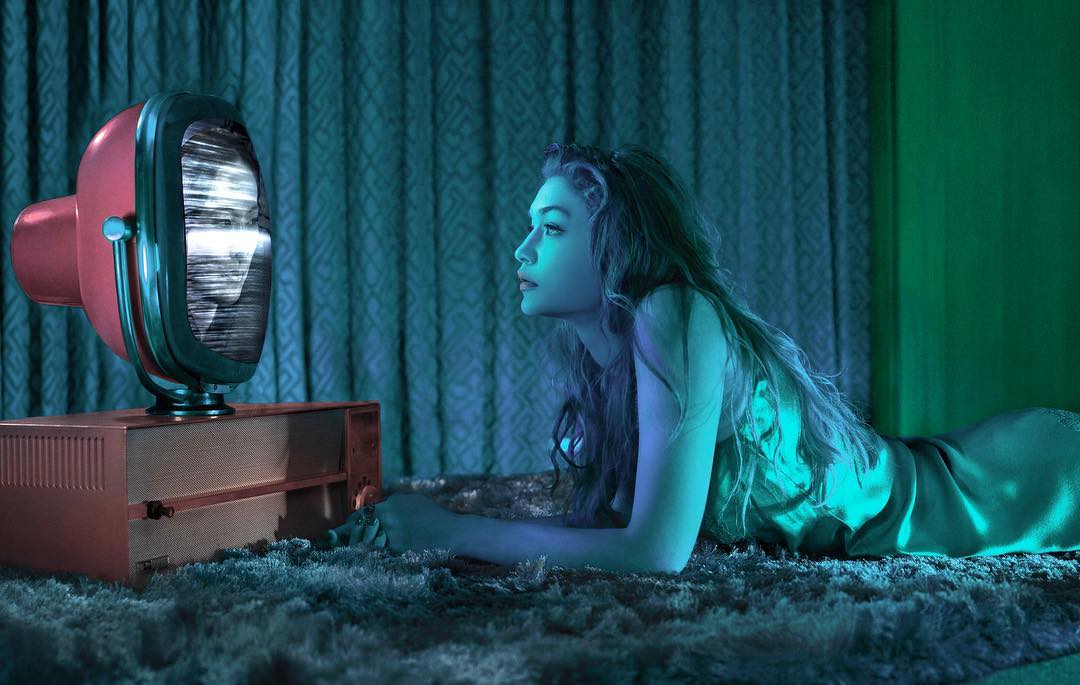 Woman lying on the floor looking at a vintage television set in a moody, dark environment with blue and green lighting.