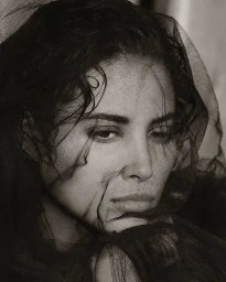 Close up portrait of a woman wearing a sheer black veil draped over her head, photographed by Albert Watson.