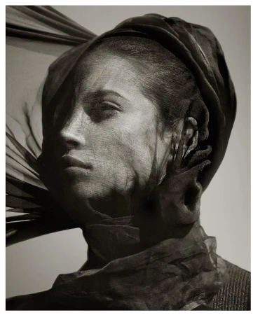 Close-up portrait of a woman wearing a dark draped headscarf and sheer veil across her face, photographed by Albert Watson.