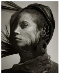 Close-up portrait of a woman wearing a dark draped headscarf and sheer veil across her face, photographed by Albert Watson.