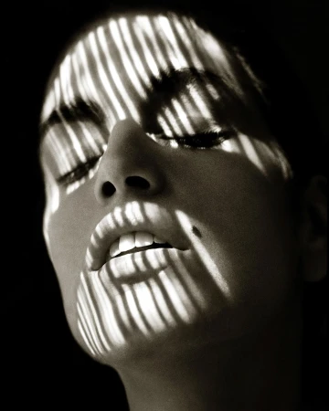Close-up portrait of a woman's face with stark striped shadows cast across her features by Albert Watson.