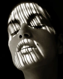 Close-up portrait of a woman's face with stark striped shadows cast across her features by Albert Watson.