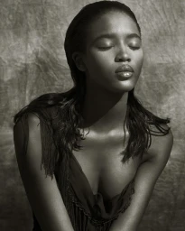 Portrait of a black woman with eyes closed wearing a dark fringed top against a textured mottled backdrop.