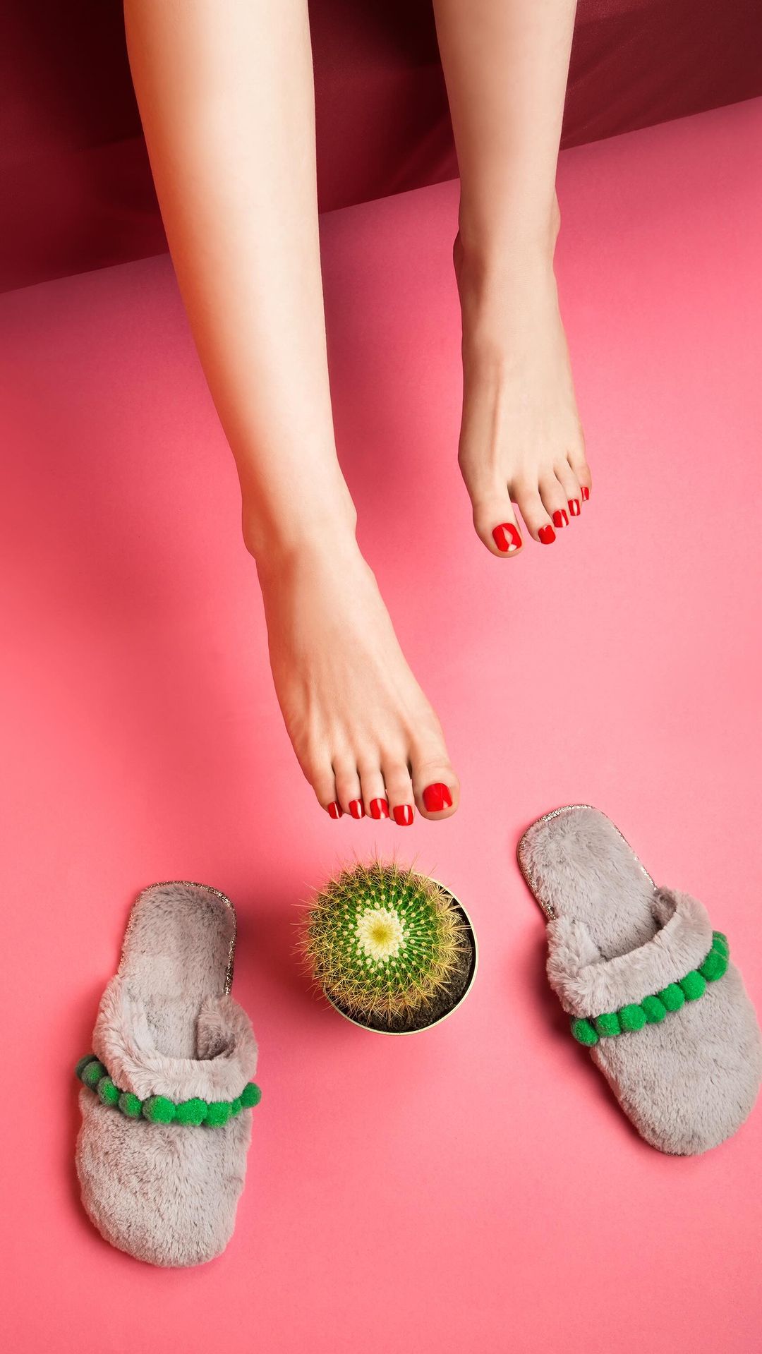 Vertical eye-level shot showcases red-toed female legs with slippers and a potted cactus against a pink backdrop, styled for a spa or beauty theme.