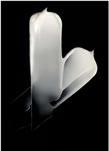 Close-up studio shot of a thick white cream swirl against a stark black background, capturing its texture and glossy appearance.