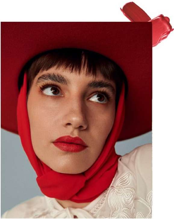 Beauty portrait of a woman with red lipstick, wearing a red scarf and hat, gazing upward against a soft blue background.