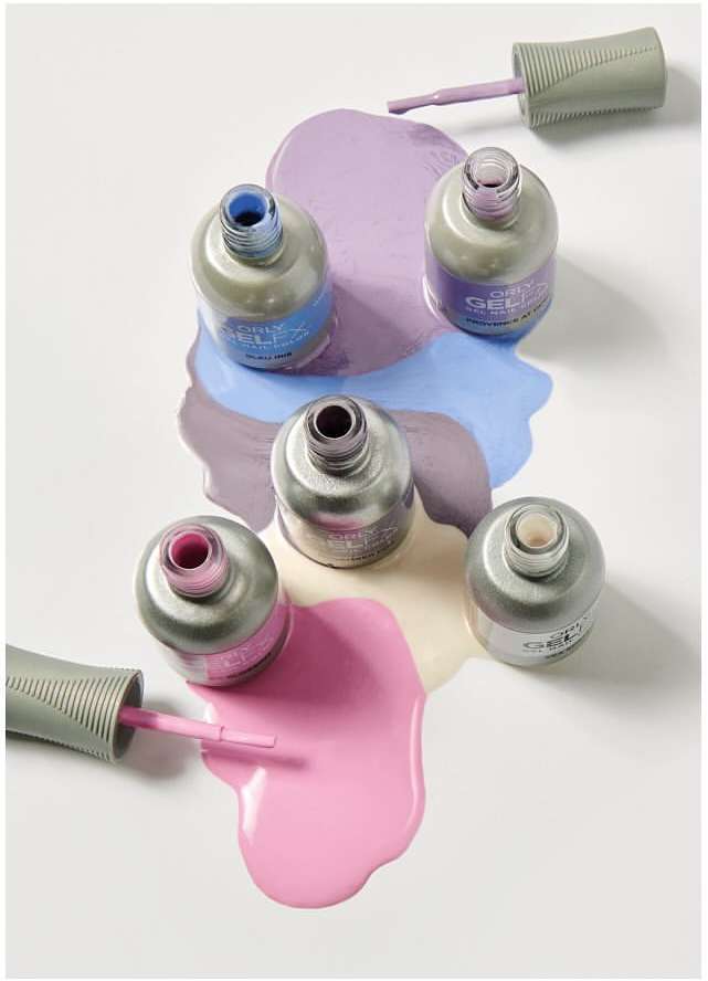 Overhead shot of five pastel nail polish bottles with caps off, surrounded by spilled polish on a clean white background.