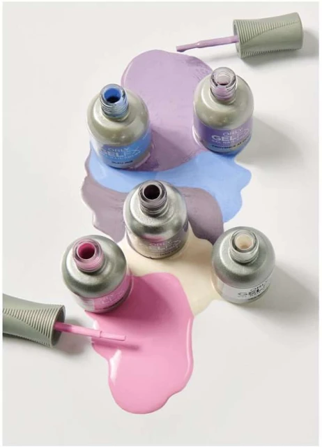 Overhead shot of five pastel nail polish bottles with caps off, surrounded by spilled polish on a clean white background.