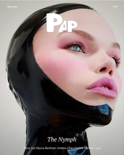 Close-up of a young woman wearing a black latex hood, pale skin, and pink makeup. Magazine cover with the masthead "PAP" and text "The Nymph."