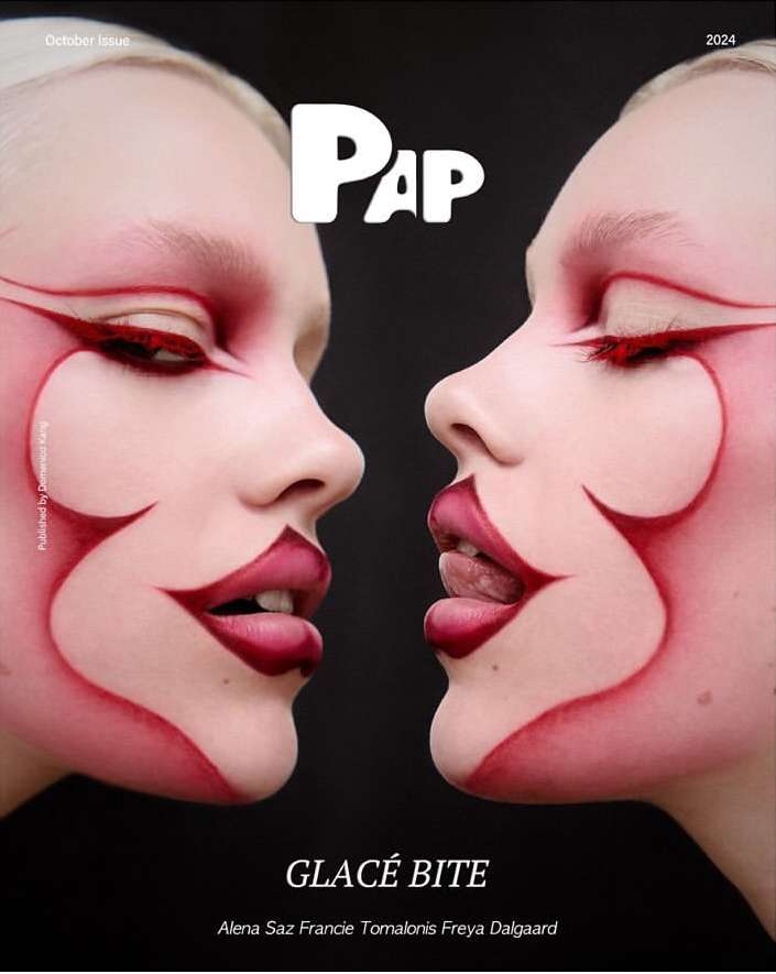 Closeup of two women with pale skin and artistic red eye and face makeup, with red lip makeup in a fashion editorial style.