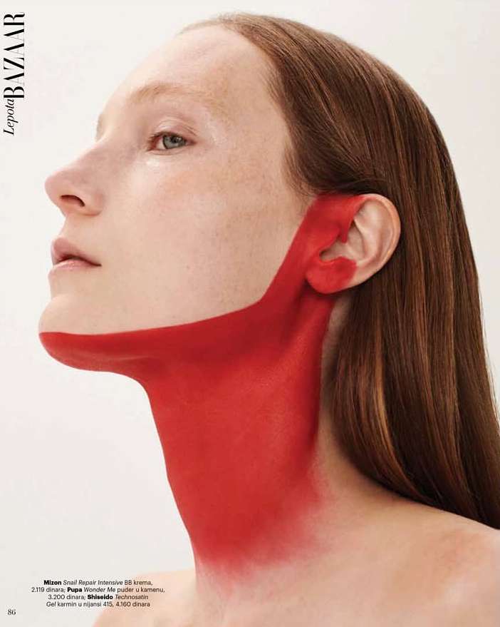 Portrait of woman with auburn hair and red paint, close-up profile view. Beauty ad in a studio with white background.
