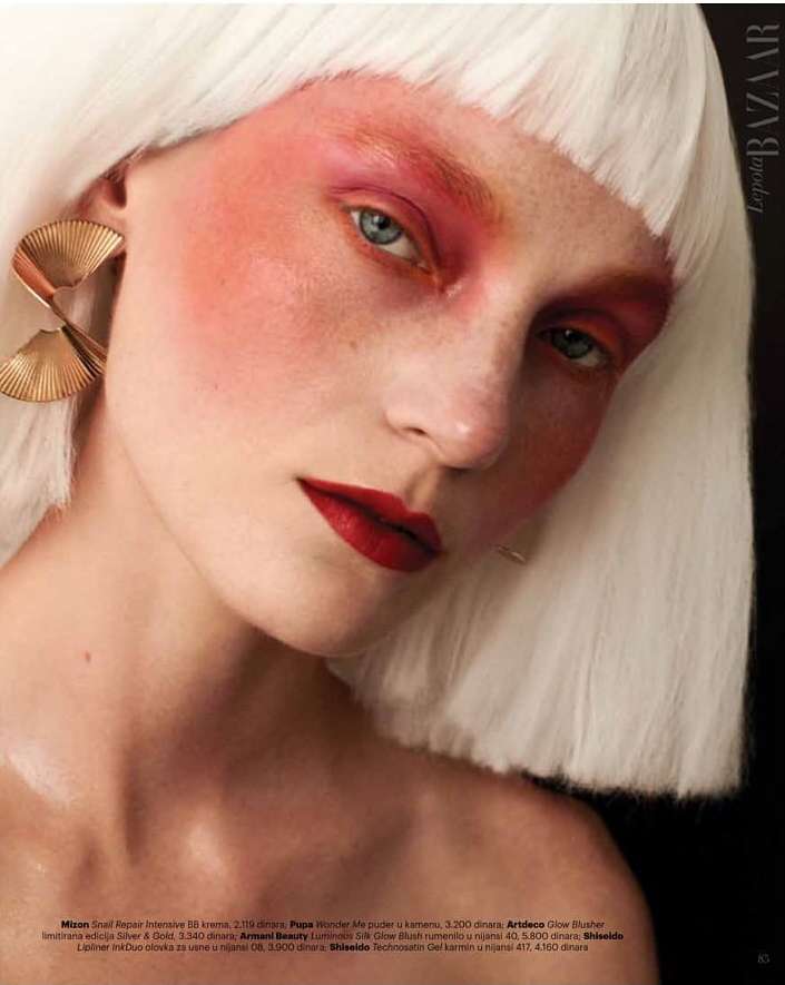 Close-up portrait of a woman with white bob wig, bold pink eyeshadow, deep red lips, and large pleated gold earrings by Alena Sazonova