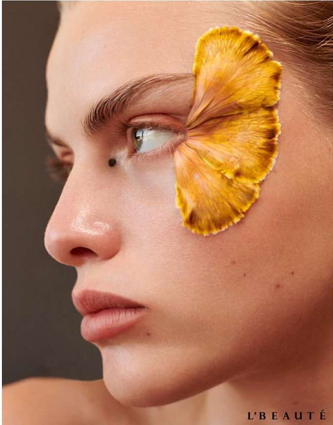 Portrait of a woman with a yellow flower petal obscuring her eye, close-up shot, beauty and cosmetics, studio lighting, neutral background.