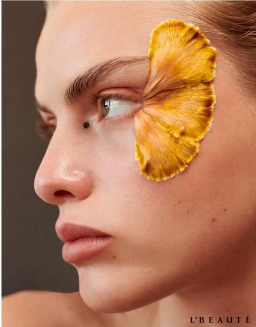 Portrait of a woman with a yellow flower petal obscuring her eye, close-up shot, beauty and cosmetics, studio lighting, neutral background.