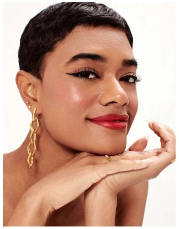 Close-up portrait of a woman with short dark hair, bold winged eyeliner, and red lipstick wearing gold geometric earrings.