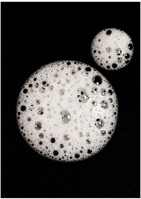 Circular formations of white foam and bubbles contrast against a black background in this macro beauty and wellness close-up.