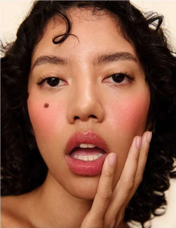 Close-up beauty portrait of a woman with curly dark hair, glossy pink lips, and a distinct mole on her cheek photographed by Alena Sazonova