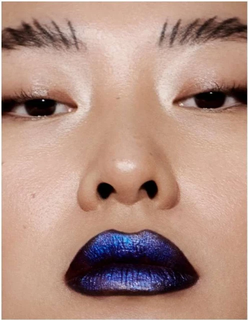 Close-up of a woman's face with blue lipstick, dark eyes, and minimalist eyebrow makeup, showcasing beauty and makeup trends.