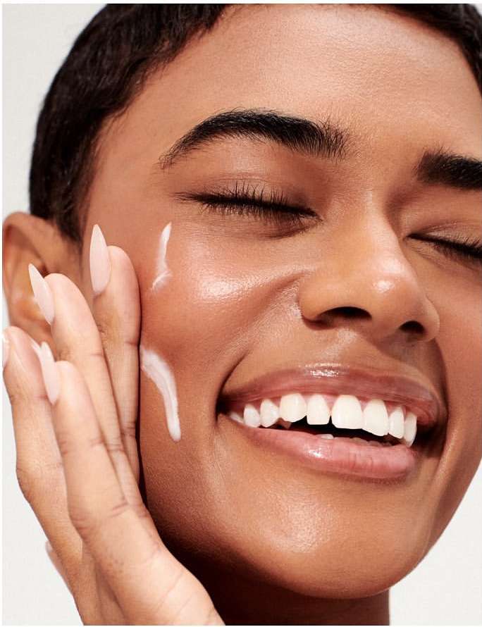 Close-up shot of an adult woman with her eyes closed, applying a white cream to her face, showcasing beauty and skincare.