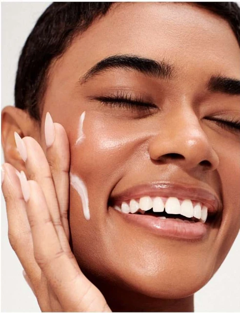 Close-up shot of an adult woman with her eyes closed, applying a white cream to her face, showcasing beauty and skincare.