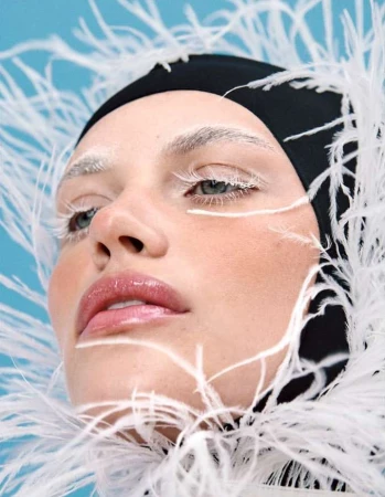 Close-up portrait of a woman wearing a black swim cap framed by fluffy white feathers against a blue background